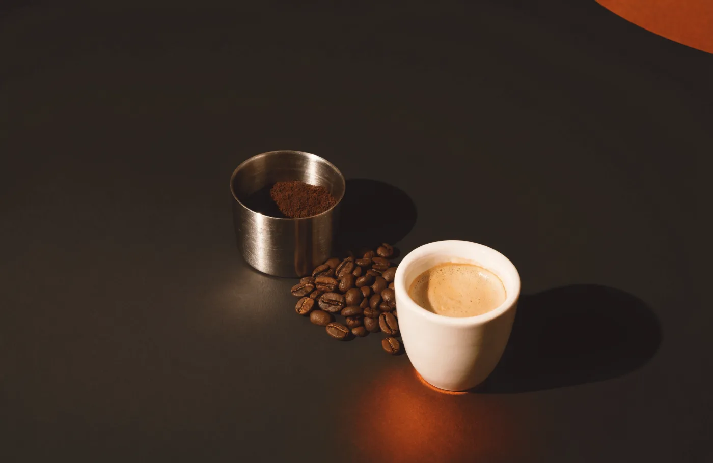 Espresso with crema beside a steel dosing cup and coffee beans