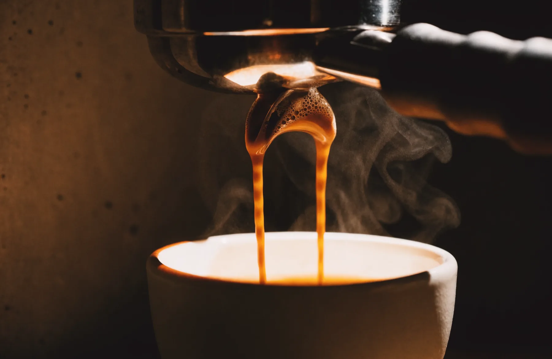 Espresso extracting from a bottomless portafilter into a cup, with steam rising